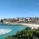 Stunning sandy beach with vibrant turquoise waters and scenic clifftop houses—ideal for a 10-day Oz Intro Sydney to Brisbane tour.