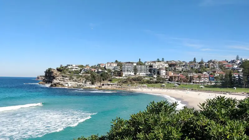 Stunning sandy beach with vibrant turquoise waters and scenic clifftop houses—ideal for a 10-day Oz Intro Sydney to Brisbane tour.