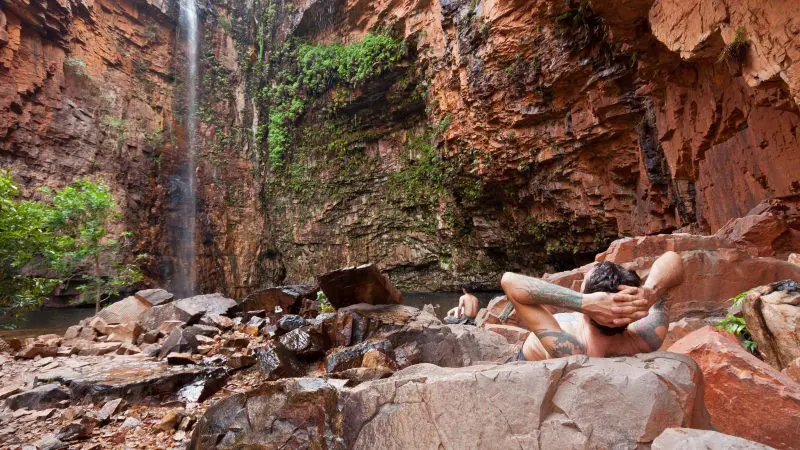 Traveller unwinds on scenic rocks by a cascading waterfall during the 10 Day Broome to Darwin 4WD Kimberley Adventure tour.