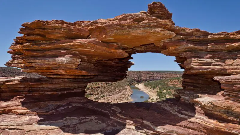 Majestic natural rock arch frames scenic river and valley on Darwin to Perth adventure tour with Broome accommodation, desert sky vista.