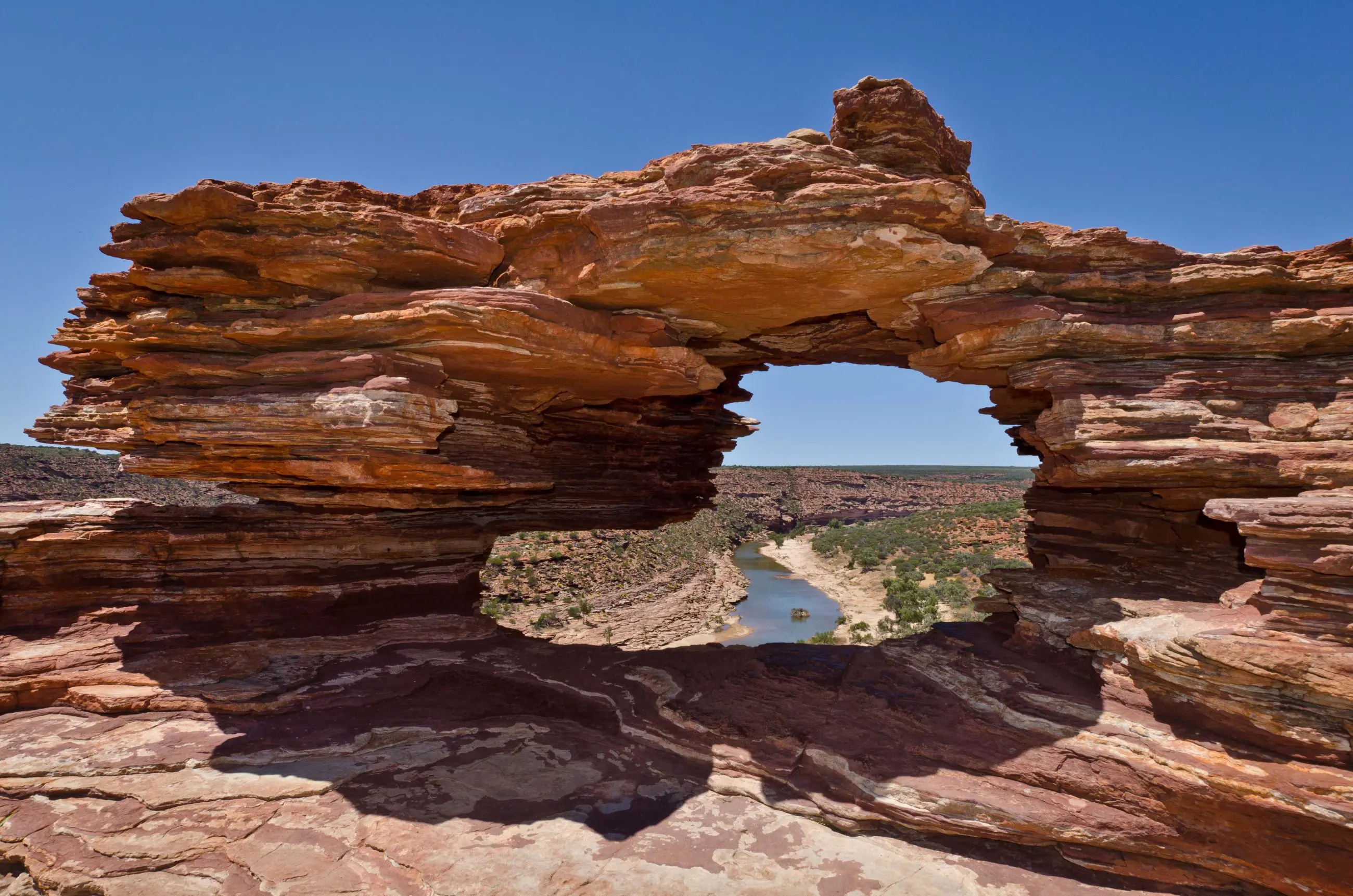 Dramatic natural rock arch overlooking winding river and rugged terrain on 10 Day Broome to Perth West Coast Adventure tour.