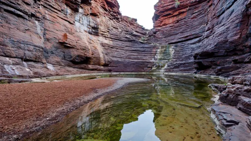 Stunning red rock gorge with dramatic layered cliffs, clear shallow waters, and scenic reflections on a Broome to Perth adventure tour.