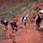 Five hikers trek a rugged, red-rock trail on a five-day Outback camping adventure loop from Alice Springs, Australia.