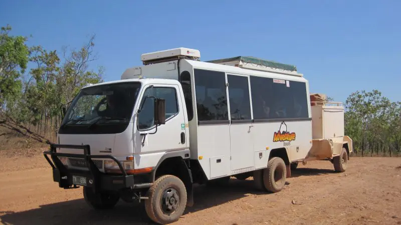 White tour coach for the 5 Day Outback Camping Adventure Yulara to Alice Springs parked on scenic rural dirt road under open sky.