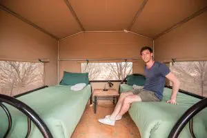 A man relaxes in a cosy tent with twin green-bedded beds on a 2-day Uluru adventure from Yulara, enjoying scenic outback comfort.