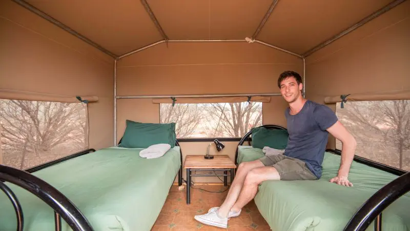 A man relaxes in a cosy tent with twin green-bedded beds on a 2-day Uluru adventure from Yulara, enjoying scenic outback comfort.