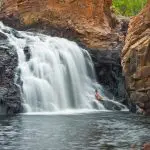 Traveller relaxing on a rock by a wide waterfall in Kakadu National Park, ideal for unforgettable tour camping and adventure experiences.