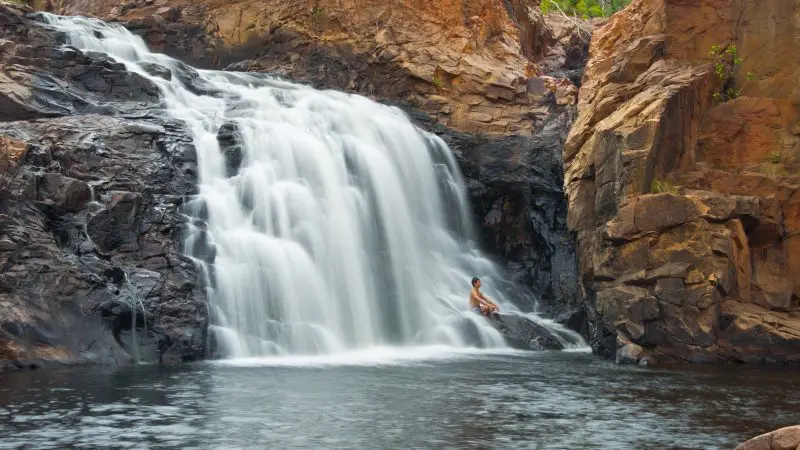 Traveller relaxing on a rock by a wide waterfall in Kakadu National Park, ideal for unforgettable tour camping and adventure experiences.