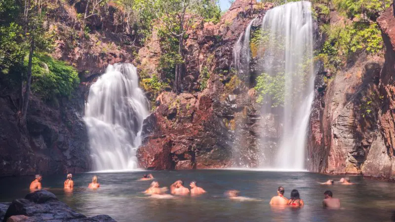 Visitors enjoy swimming in a crystal-clear natural pool at Twin Waterfalls, Kakadu, encircled by dramatic cliffs and verdant rainforest.