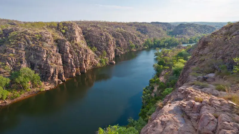 Embark on a Kakadu 4WD adventure: discover a winding river, striking rocky cliffs, and lush greenery beneath dramatic clouded skies.