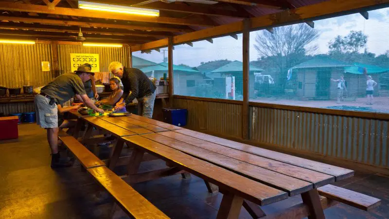 Four people cooking together on a long table during a 3-night Uluru tour from Alice Springs to Yulara, Australian Outback adventure.