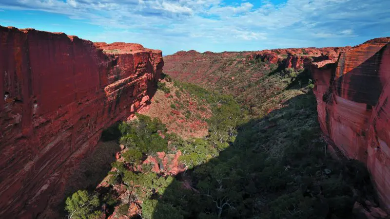 Majestic canyon with towering red rock cliffs and verdant trees—iconic landscape for a 3 Day Uluru Adventure Alice Springs return.