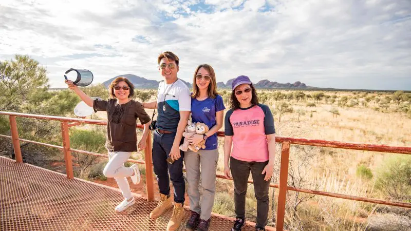 Four happy travellers pose on a metal platform during a 3-night Uluru tour from Alice Springs to Yulara, showcasing adventure joy.