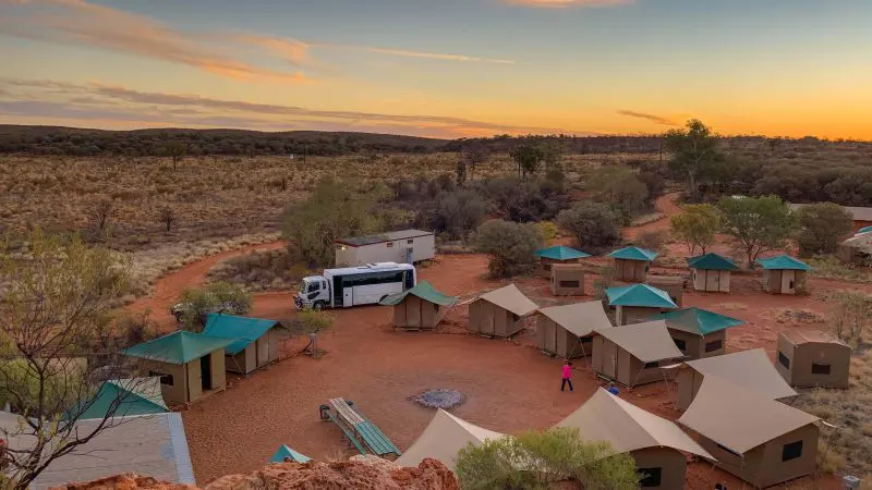 Experience a scenic campsite with vibrant green-roofed tents and a white tour coach on the 3 Night Uluru Adventure from Alice Springs to Yulara.