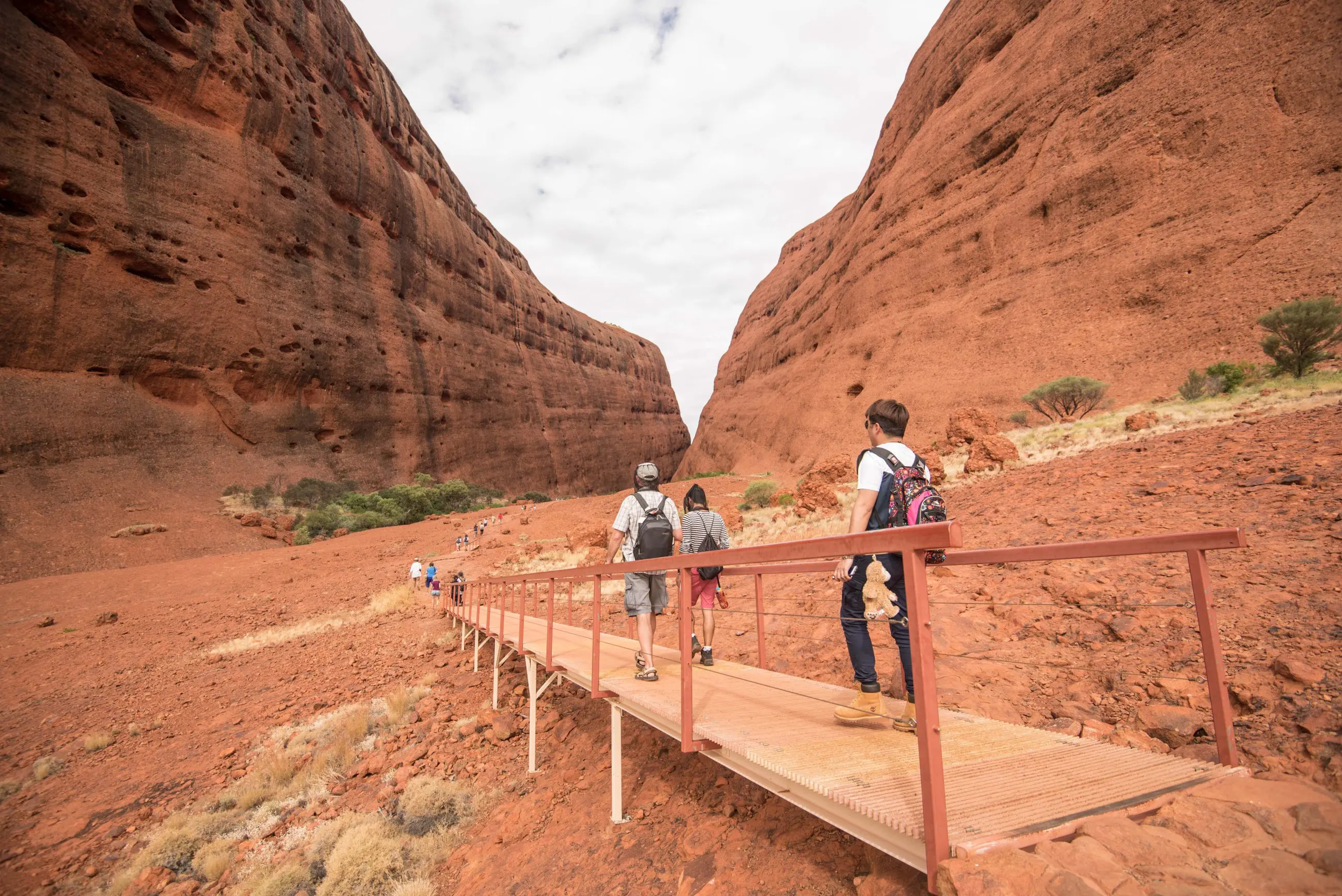 Travellers exploring a scenic boardwalk through Uluru’s stunning red canyon on a 3-day adventure from Yulara to Alice Springs.