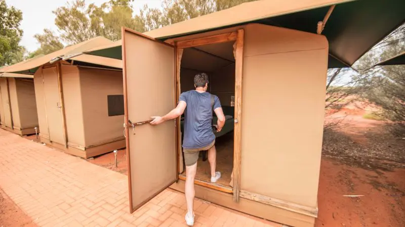 Traveller arrives at a tan canvas tent cabin during a 3-night Uluru Adventure tour from Alice Springs to Yulara, outback Australia.
