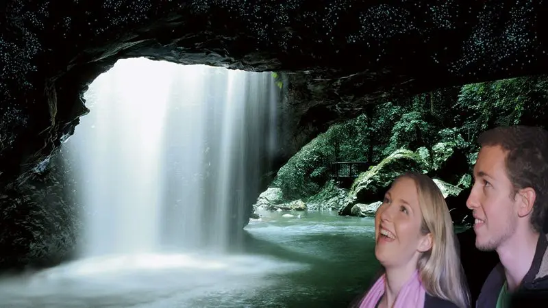 Smiling couple pose by a stunning cave waterfall during a popular Natural Bridge Glow Worm Night Tour from the Gold Coast, Australia.