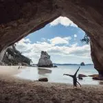 A joyful person stands on a sandy beach, arms raised towards the sky, enjoying a vibrant sea view and sunny coastal atmosphere.