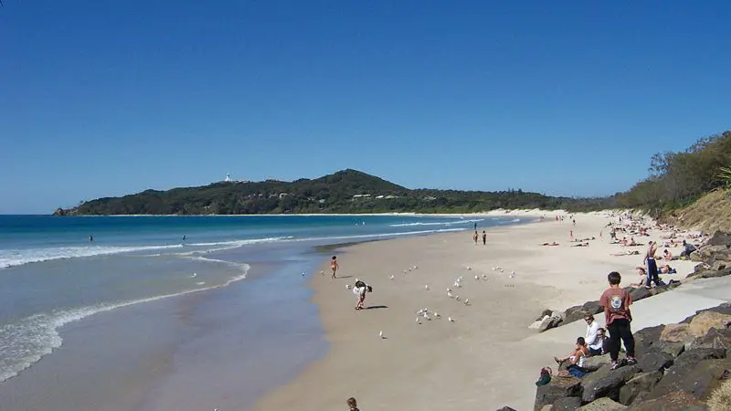 Tourists relaxing on Byron Bay’s pristine sandy beach, enjoying sunshine, gentle waves, and a clear blue sky for the perfect holiday.