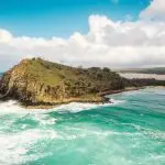 Scenic rocky island with vibrant greenery and crystal-clear turquoise waves on a K'gari 2 Day Tour from Hervey Bay beneath cloudy skies.