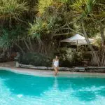 Woman in white swimming costume stands by luxury pool, surrounded by lush tropical greenery on Kgari 5 Day Ultimate Escape holiday.