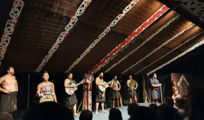 Diverse group of talented performers engaging the audience on a brightly lit stage during a live theatrical or musical performance.