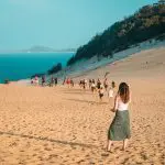 Woman strolling along pristine sandy beach towards a group, enjoying the Fully Guided Ultimate East Coast Sydney to Cairns 3 Weeks tour.