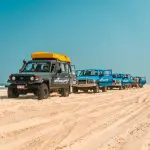 Experience the thrill of four 4WD vehicles driving along a pristine sandy beach beneath clear blue skies on the Sydney to Cairns tour.
