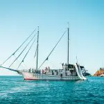 Luxury white sailing boat with passengers and fun slide anchored by scenic rocks on Sydney to Cairns 3-week guided East Coast tour.