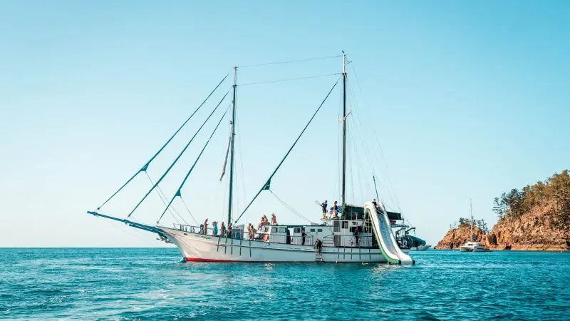 Luxury white sailing boat with passengers and fun slide anchored by scenic rocks on Sydney to Cairns 3-week guided East Coast tour.