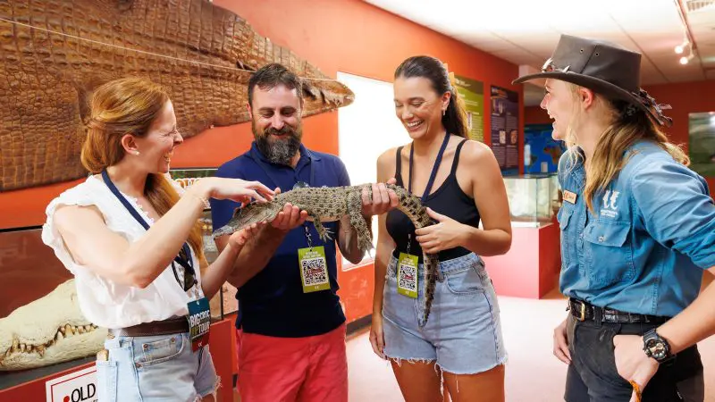 Group of four visitors smiling whilst holding a small crocodile inside Croc N History Explorer, surrounded by engaging museum exhibits.