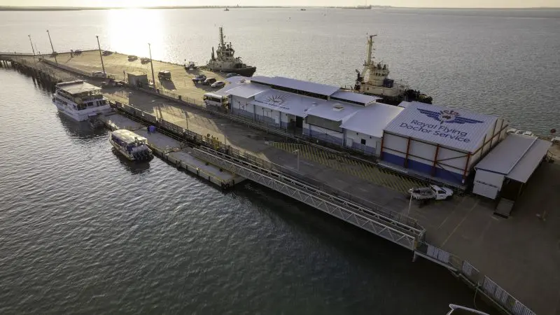 Stunning aerial view of Darwin dock with boats, RFDS Aviation Attraction Ticket building, and vibrant sunset reflecting on the waterfront.