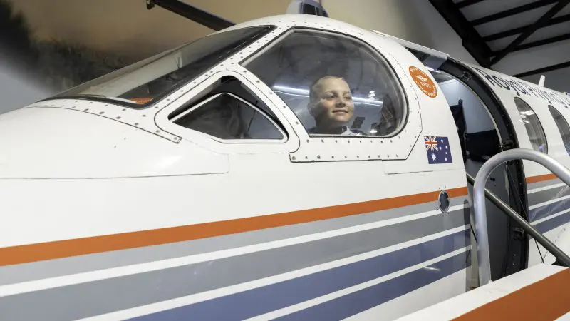 Smiling pilot inside a small white aeroplane featuring Australian flag decals at RFDS Darwin Tourist Facility, Northern Territory.