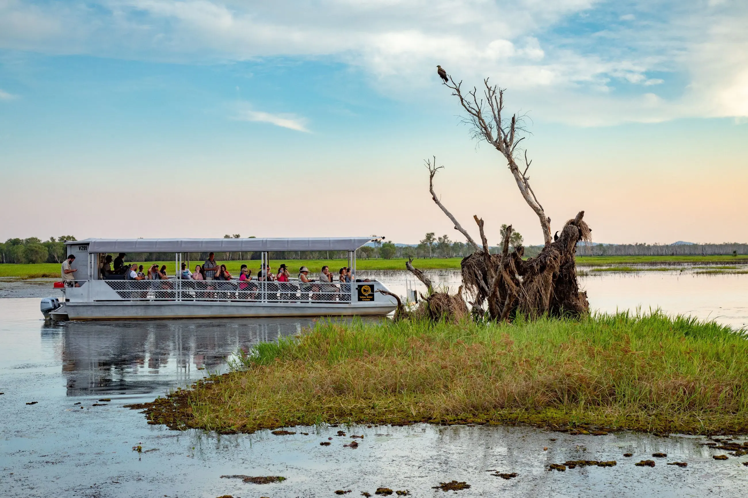 Tour boat glides through Kakadu wetlands at sunset on the 2 Day Outback Retreat from Darwin, beneath vibrant blue skies.