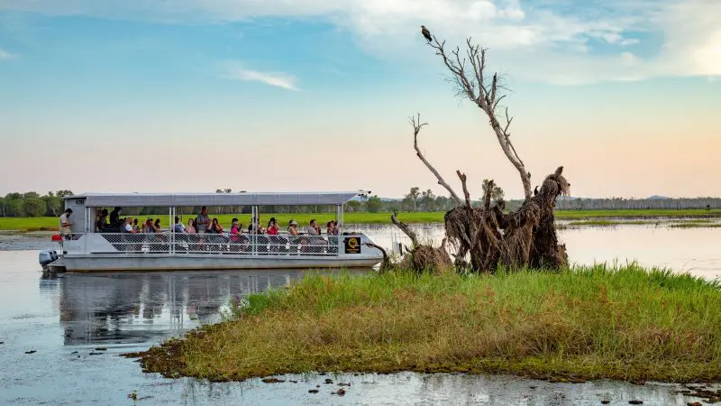 Tour boat glides through Kakadu wetlands at sunset on the 2 Day Outback Retreat from Darwin, beneath vibrant blue skies.