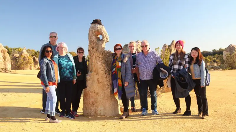 Happy travellers gather by a striking rock on their 4 Day Perth to Monkey Mia Coastal Loop Return Tour, capturing scenic moments together.