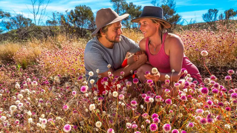 Joyful couple in hats smiles amid vibrant pink wildflowers during a sunny Pinnacles Lobster Lavender Day Tour from Perth.