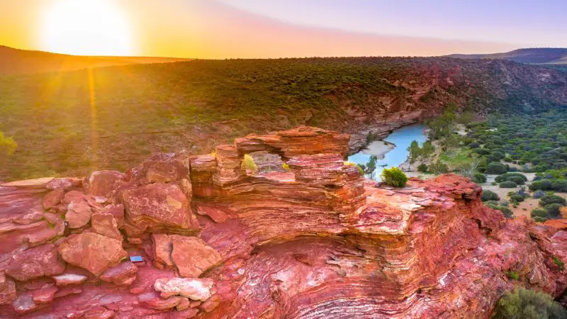 Striking red sandstone cliffs rise above a scenic winding river, seen along the iconic 6 Day Perth to Exmouth Coral Coaster tour route.