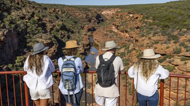 Four friends wearing hats and rucksacks overlook a stunning red rock canyon on the 6 Day Perth to Exmouth Coral Coaster tour adventure.