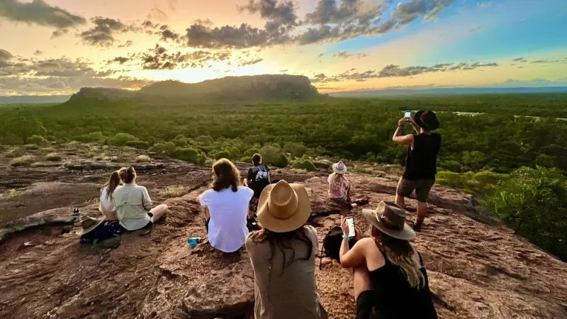 Travellers watch a vibrant sunset atop a rocky hill during the 3 Day Kakadu Litchfield National Park 4WD Safari adventure tour.