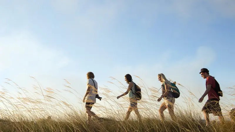 Adventurers with rucksacks hike through lush grass on a 5-day Kakadu, Katherine Gorge, and Litchfield 4WD tour from Darwin.