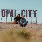 Two happy travellers pose by a giant OPAL CITY sign on a 7 Day Adelaide to Uluru Adventure with Untamed Escapes tour in Australia.