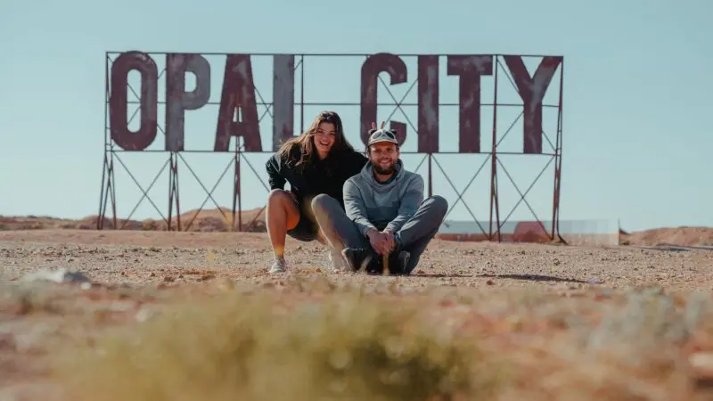 Happy couple by iconic OPAL CITY sign during their immersive 7-Day Uluru to Adelaide tour with Untamed Escapes, Australia adventure.