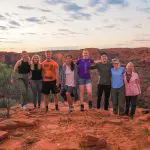 Group of eight adventurers smiling on a rocky sunset cliff during a 7 Day Adelaide to Uluru Untamed Escapes tour experience.
