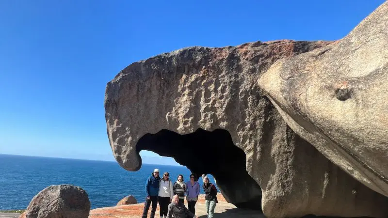 Group of six travellers by the ocean under iconic Kangaroo Island rock formation and blue sky on Untamed Escapes 3 day tour adventure.