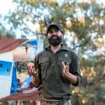 Bearded man sharing insights by the Adnyamathanha Flag during the 7 Day Adelaide to Uluru Adventure tour with Untamed Escapes.