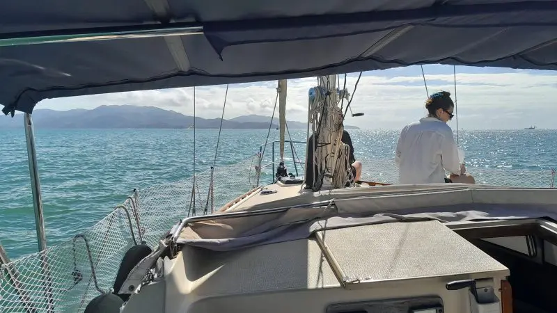 Experience a Townsville Lunchtime Sailing Private Charter as two people unwind on a sailboat, with tranquil blue waters and scenic mountains.