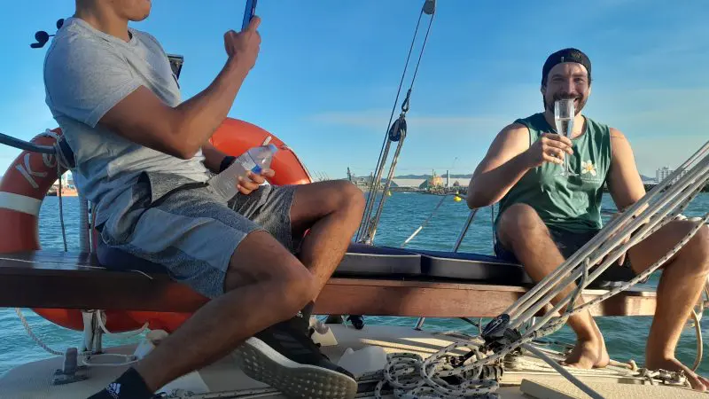 Two men enjoy a scenic Townsville Lunchtime Sailing Private Charter; one captures the view while the other smiles, drink in hand.