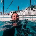 A happy swimmer enjoys crystal-clear Whitsunday waters near New Horizon during a 2 Day 2 Night sailing adventure under sunny skies.