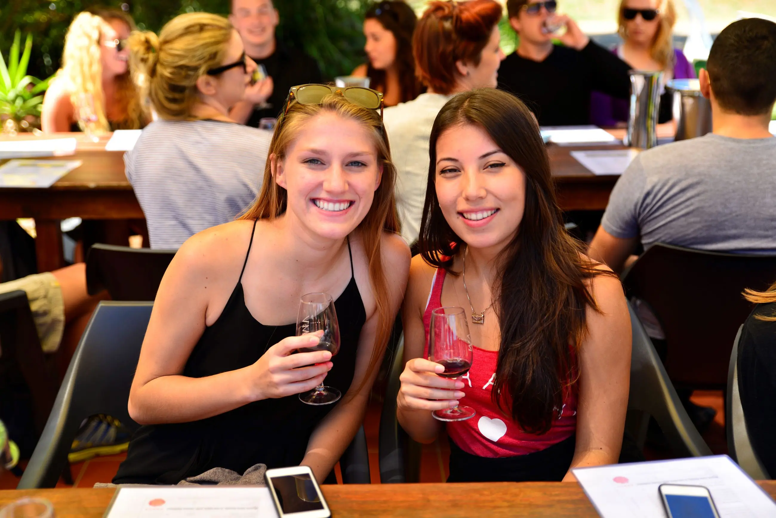 Two young women savour wine outdoors at a 1 Day Hunter Valley Wineries Tour from Sydney, surrounded by scenic vineyard views.